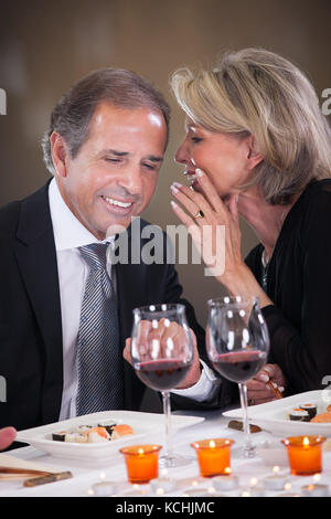 Fröhliche Frau flüstert etwas im Ohr des Menschen in einem eleganten Restaurant Stockfoto