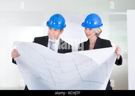 Ältere Ingenieure bei Blueprint tragen, hardhat im Büro Stockfoto