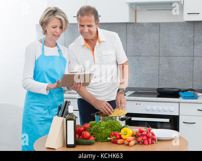 Reifer Mann und Frau betrachten Rezept Tablet beim Kochen In der Küche Stockfoto