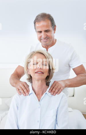 Reifer Mann massiert die Schulter der Frau im Bett Stockfoto