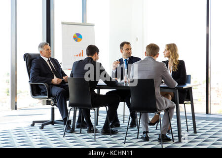 Die Leute sitzen rund um Tisch, Reden und Arbeiten mit Dokumenten Stockfoto