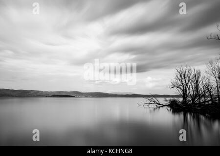 Langzeitbelichtung, Blick auf den See, mit perfekt noch Wasser, Skelett Bäume und ziehenden Wolken Stockfoto