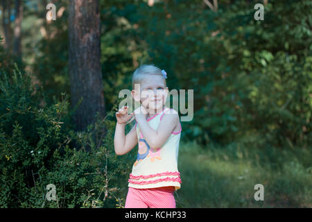 Wenig schöne blonde Kind stehen im Wald. Sie glättet Ihr Haar und lächelnd Stockfoto