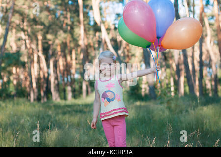 Kleine blonde Mädchen im Wald. Hält sie ein einen Armful bunte Luftballons Stockfoto