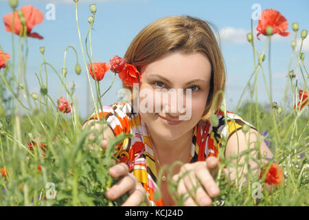 Schöne Mädchen mit Blumen geschmückten Bluse mit Lächeln unter Mohn Blumen posing Stockfoto