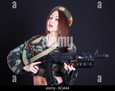 Schöne junge Frau in einer Uniform mit einem Sturmgewehr auf schwarzem Hintergrund Stockfoto