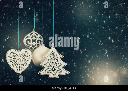 Christbaumschmuck und Kugeln hängen vor einem blauen Hintergrund aus Holz mit Schnee und leuchten Bokeh. Filmkorn hinzugefügt Stockfoto