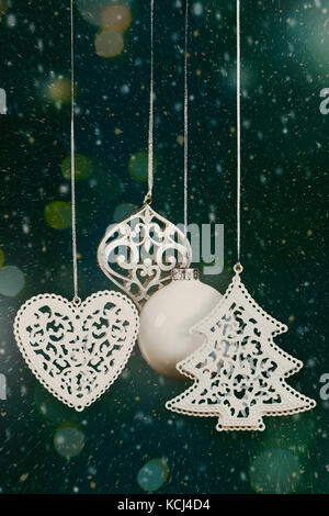 Weihnachtsbaumschmuck und Kugeln hängen vor einem grünen Hintergrund mit Schnee, Bokeh Lichter und Funken. Filmkörnung hinzugefügt Stockfoto