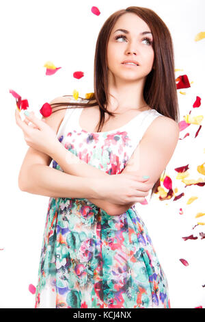 Portrait von eine hübsche junge Frau in einem hellen Kleid mit weißem Hintergrund mit Rosa und Gelb fallende Blütenblätter isoliert Stockfoto