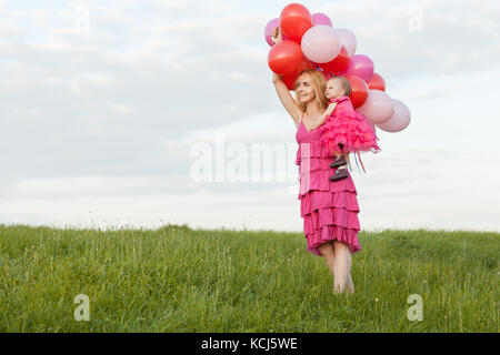 Mama hält eine Tochter und Luftballons in den Händen. Sie sehen Stockfoto