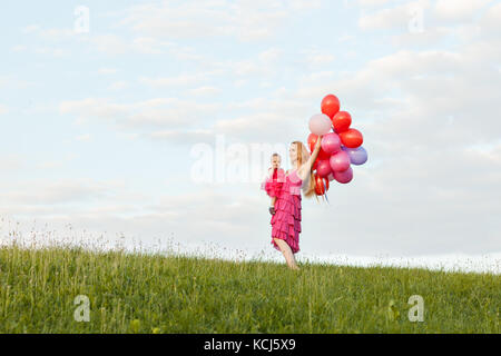 Mutter und Tochter in hellen Kleidern auf die Skyline stehen. Mama hält ein Bündel Luftballons in den Händen Stockfoto