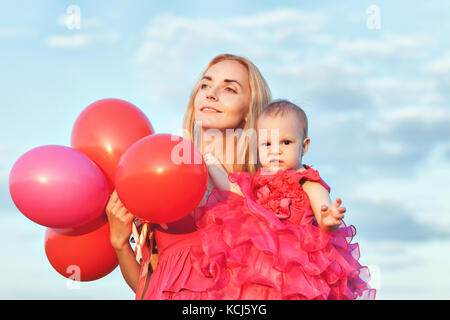 Mama hält eine Tochter und ein Bündel Luftballons in ihre Arme Stockfoto