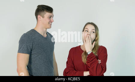 Hübsches Mädchen flüstert Geheimnis im Ohr ihres lachenden Freundes auf weißem Hintergrund - Freundschaftskonzept Stockfoto