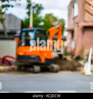 Abstrakte verschwommenen Hintergrund - kleine Bagger mit Mann nach Innen, in der Arbeit, die Straße zu reparieren. Stockfoto