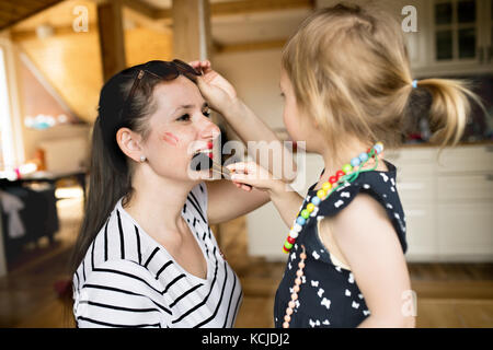 Süße kleine Mädchen zu tun - bis zu Ihren attraktiven Mom mit der Bürste. Stockfoto