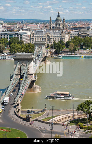 Eine Luftaufnahme der Széchenyi Kettenbrücke, aufgenommen von der Budaer Burg mit der St. Stephens Basilika im Hintergrund an einem sonnigen Tag mit blauem Himmel. Stockfoto