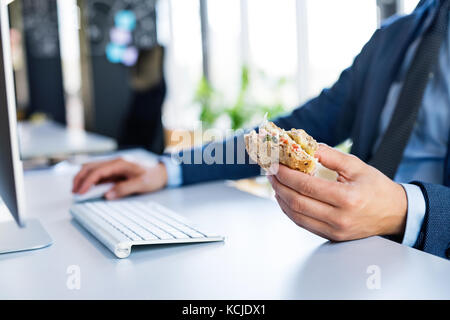 Geschäftsmann an einem Schreibtisch mit Computer zu Mittag gegessen. Stockfoto