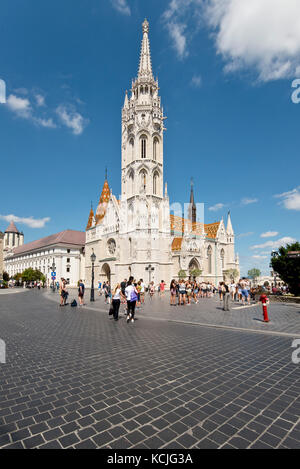 Blick auf die Matthias-Kirche auf dem Burgberg mit Touristen, die an einem sonnigen Tag mit blauem Himmel herumlaufen. Stockfoto