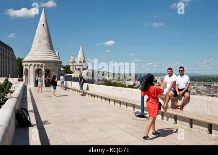 Touristen an den Wänden der Fischerbastei in Budapest betrachten die Aussicht und fotografieren Fotos an einem sonnigen Tag mit blauem Himmel. Stockfoto