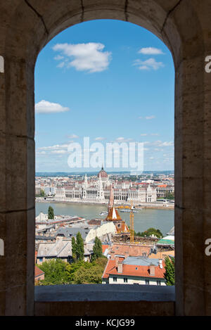 Der Blick durch eines der "Fenster" auf die Fischerbastei mit dem ungarischen Parlamentsgebäude an einem sonnigen Tag mit blauem Himmel. Stockfoto