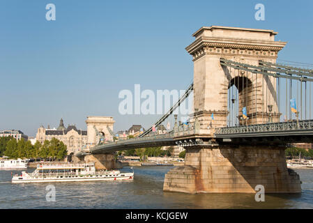 Ein Blick auf die Széchenyi Kettenbrücke in Budapest mit einer Tagesfahrt Flusskreuzfahrt Boot unter an einem sonnigen Tag mit blauem Himmel vorbei. Stockfoto