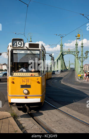 Die ganz CSMG-Straßenbahn in Budapest überquert die Freiheitsbrücke an einem sonnigen Tag mit blauem Himmel. Stockfoto