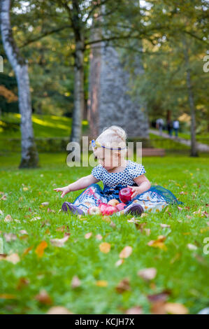 Baby Mädchen sitzen auf dem Gras und spielte mit ihren Äpfeln Stockfoto