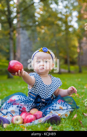 Baby Mädchen sitzen auf dem Gras und spielte mit ihren Äpfeln Stockfoto