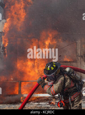 Lissabon, NH, USA. 5. Okt. 2017. Ein Feuerwehrmann mit der Lissabonner Feuerwehr schlachten Hitze, Flammen und schweren Spray extra Wasserleitungen zu tragen ein Haus Feuer unbekannter Herkunft in die Innenstadt von Lissabon, NH, USA zu kämpfen. Glücklicherweise waren keine Menschen getötet oder verletzt. Credit: Kunst Phaneuf/Alamy leben Nachrichten Stockfoto