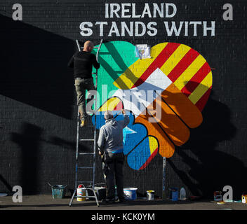 Belfast, Nordirien. Oktober 2017. Zwei irische republikanische Kunstaktivits greifen auf eine Mauer an der „International Wall/Divis Street“ zurück, um die Indepedenzbewegung in Katalonien, in Belfast, Nordirien, am 5. Oktober 2017 zu unterstützen. Die Briefe lauten: "Irland steht mit Katalonien". Quelle: Christian Charisius/dpa/Alamy Live News Stockfoto