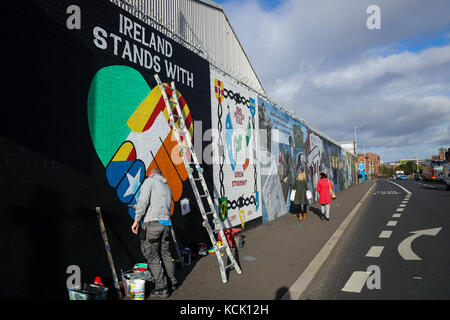 Belfast, Nordirien. Oktober 2017. Zwei irische republikanische Kunstaktivits greifen auf eine Mauer an der „International Wall/Divis Street“ zurück, um die Indepedenzbewegung in Katalonien, in Belfast, Nordirien, am 5. Oktober 2017 zu unterstützen. Die Briefe lauten: "Irland steht mit Katalonien". Quelle: Christian Charisius/dpa/Alamy Live News Stockfoto