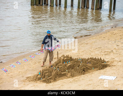 Sand Bildhauer und seine Sandburg Skulptur, mit kleinen Union Jack Fahnen, auf einem städtischen Strand neben der Themse. South Bank, London, England, UK. Stockfoto