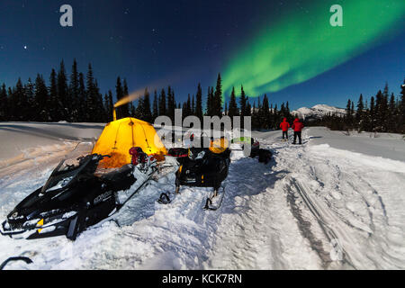 Die für die Nacht gezelteten Schneemobilfahrer werden während der Fahrt auf dem North Canol Heritage Trail, Yukon Territory, Kanada, mit Nordlichtern begrüßt Stockfoto