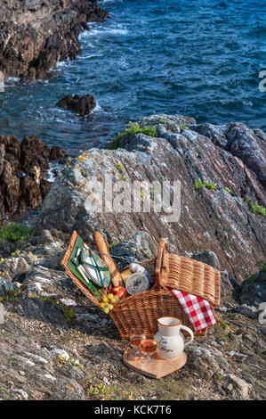 Picknickkorb mit typisch französischem Baguette und rosè Wein auf ‘abseits von allem’ küstennahen Felsvorsprung Doëlan Finistere Brittany France Stockfoto