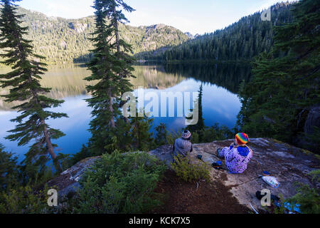 Zwei Freundinnen, die am Bedwwell Lake campen, genießen einen Kaffee am frühen Morgen. Strathcona Park, Central Vancouver Island, British Columbia, Kanada Stockfoto