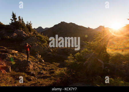 Ein eineineinter Wanderer blickt auf einen frühen Morgenaufgang, der Flower Ridge, Strathcona Park, Central Vancouver Island, British Columbia, Kanada, beleuchtet Stockfoto