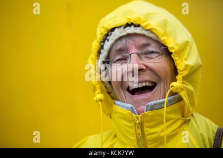 Eine glückliche, lachende älterer Bürger gekleidet in ihren gelben rain Slicker genießt das stürmische Wetter, während Sie an Bord der MV uchuck iii, freundlich Cove, Vancouver Island, British Columbia, Kanada. Stockfoto
