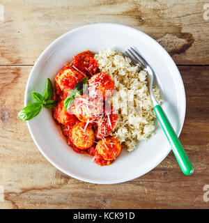 Frikadellen aus Ricotta-Käse und gekochten Reis mit Tomatensauce auf Holztisch. die Hände von Frauen Stockfoto