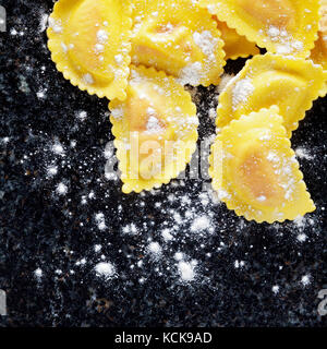 Köstliche frisch zubereitete hausgemachte Ravioli auf dunklem Marmor Oberfläche. Eier, Mehl und Basilikum. Konzept der italienischen gesundes Essen Stockfoto