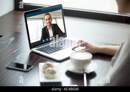 Frau, die mit einem Mann über Kopfhörer per Videoanruf spricht. Kollegen aus der Ferne chatten, lernen und tauschen Fremdsprachen aus, Mädchen beobachten Geschäftswebin Stockfoto