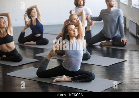 Gruppe junge sportliche Menschen üben Yoga Lektion mit Kursleiter, Stretching in einem vierbeinigen King pigeon Übung Eka Pada rajakapotasana darstellen, worki Stockfoto