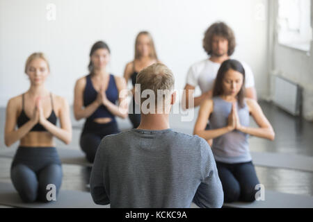 Gruppe junge sportliche Menschen üben Yoga Lektion mit Instructor, vajrasana Übung sitzen, Seiza darstellen, Indoor, Studio, Rückansicht Stockfoto