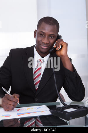 Junge afrikanische Unternehmer holding Stift über Grafik Gespräch am Telefon Stockfoto