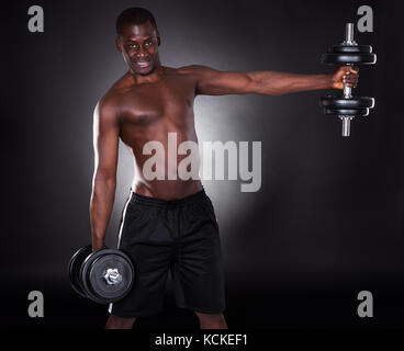 Porträt der jungen afrikanischen Mann heraus arbeiten mit Kurzhanteln auf schwarzem Hintergrund Stockfoto
