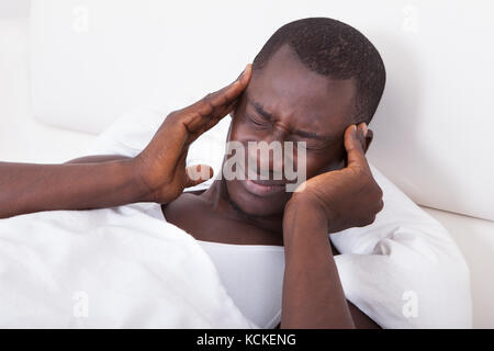 Junge Afrikaner mit Kopfschmerzen auf Bett liegend Stockfoto