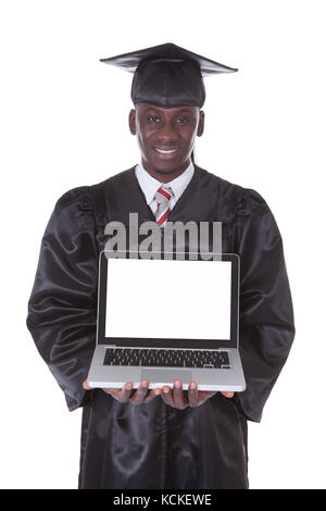 Junger Mann In der Graduierung Robe zeigt Laptop Over White Background Stockfoto