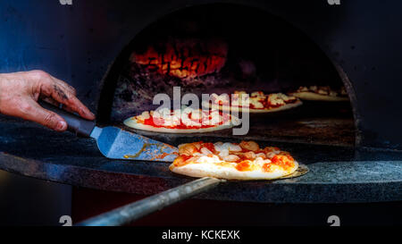 Der Küchenchef seine Pizza Kochen in einem mit Holz befeuerten Ofen Inspektion an einer italienischen Festival. Stockfoto