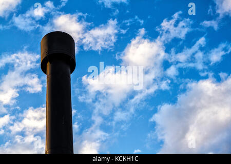 Low Angle View eines schwarzen Schornstein gegen den blauen Himmel mit einigen Wolken. Stockfoto