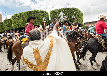 Mexikanischen Cowboys sind mit Weihwasser besprengt durch katholische Priester den Segen ihrer Wallfahrt während des Festivals von St. Michael in San Miguel de Allende, Mexiko. Stockfoto