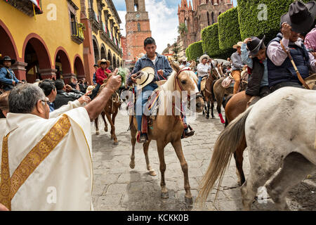 Mexikanischen Cowboys sind mit Weihwasser besprengt durch katholische Priester den Segen ihrer Wallfahrt während des Festivals von St. Michael in San Miguel de Allende, Mexiko. Stockfoto